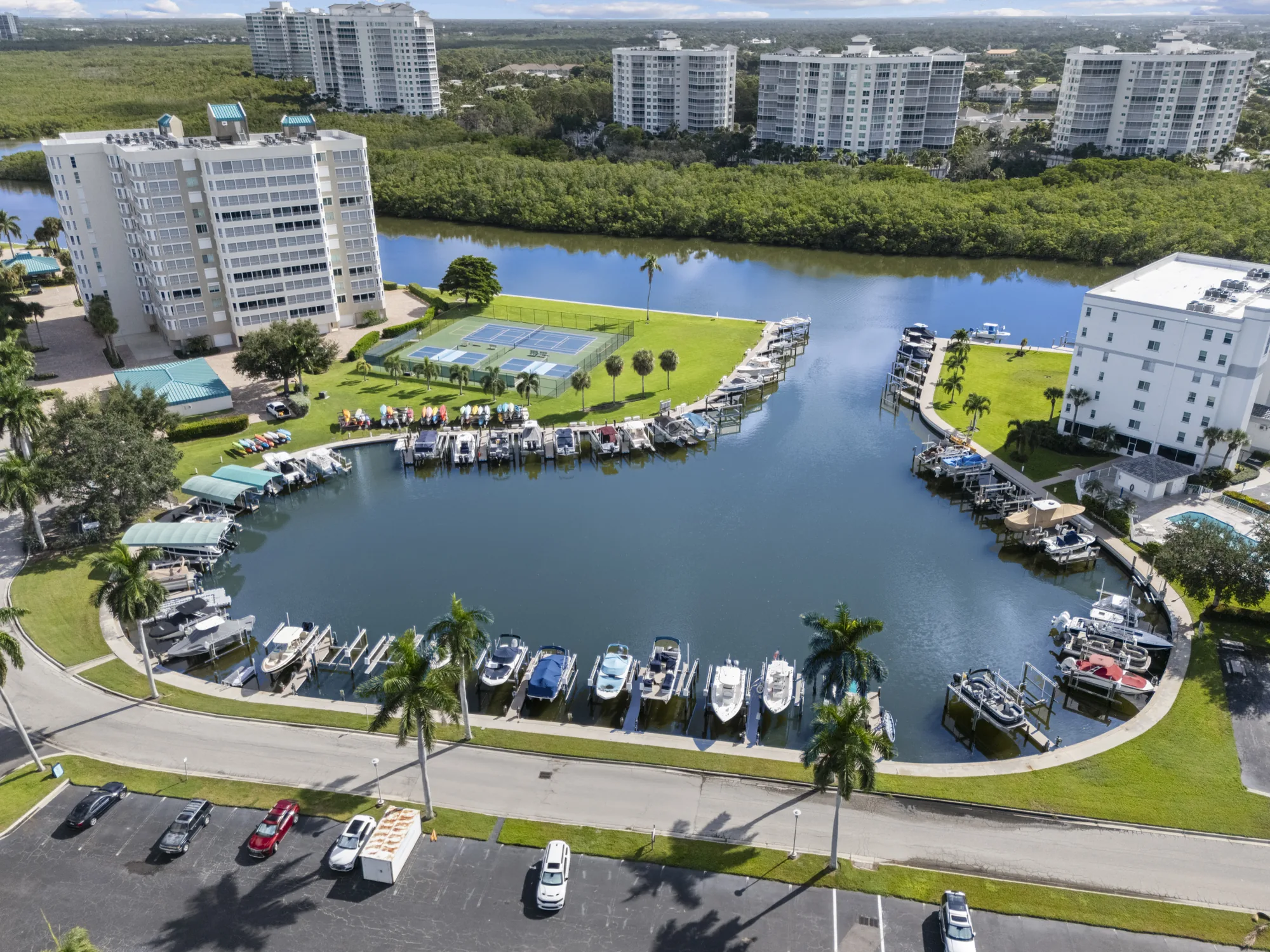 Aerial of the marina basin on Bluebill Avenue beside Gulf Breeze at Vanderbilt, with boat docks and lifts, tennis and pickleball courts and the mangroves beyond, Vanderbilt Beach, Naples, Florida