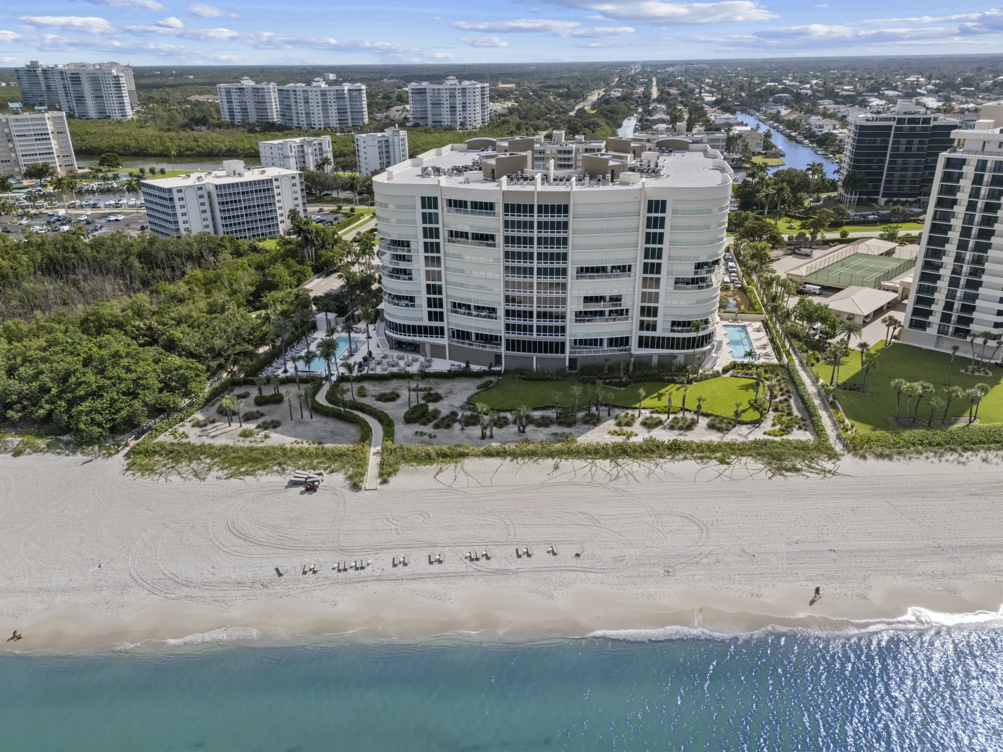 Aerial of Moraya Bay from the Gulf, the eleven-story beachfront high-rise above its two pools, gardens and the sand at the north end of Vanderbilt Beach, Naples, Florida