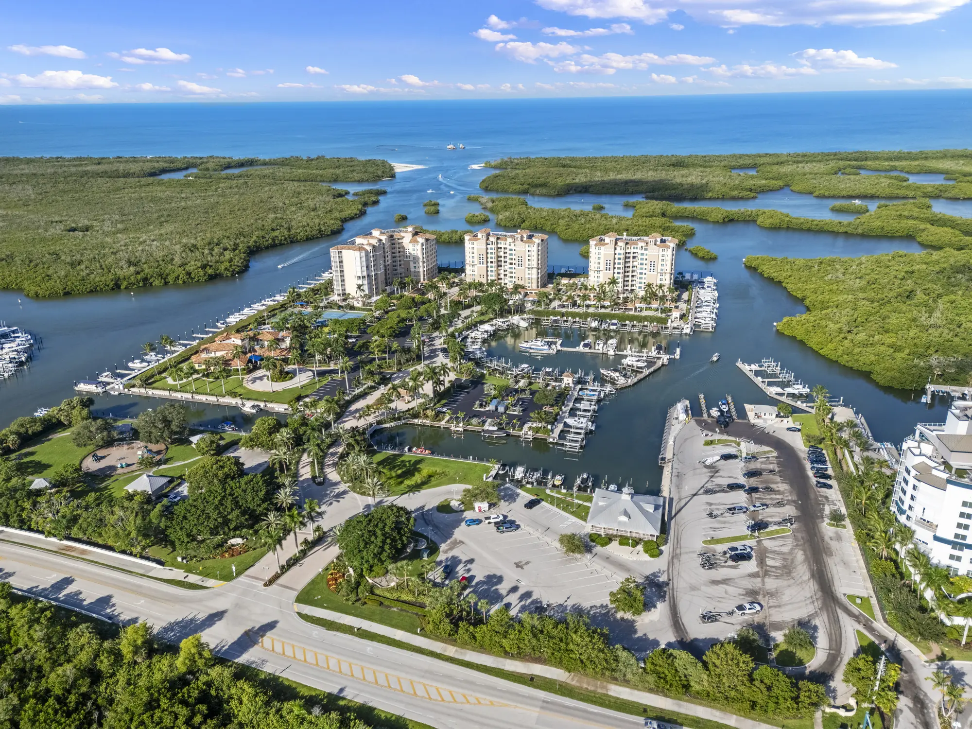 Aerial of the Pelican Isle Yacht Club marina and towers on Wiggins Pass, with the Cocohatchee River Park public boat ramp and parking in the foreground, North Naples