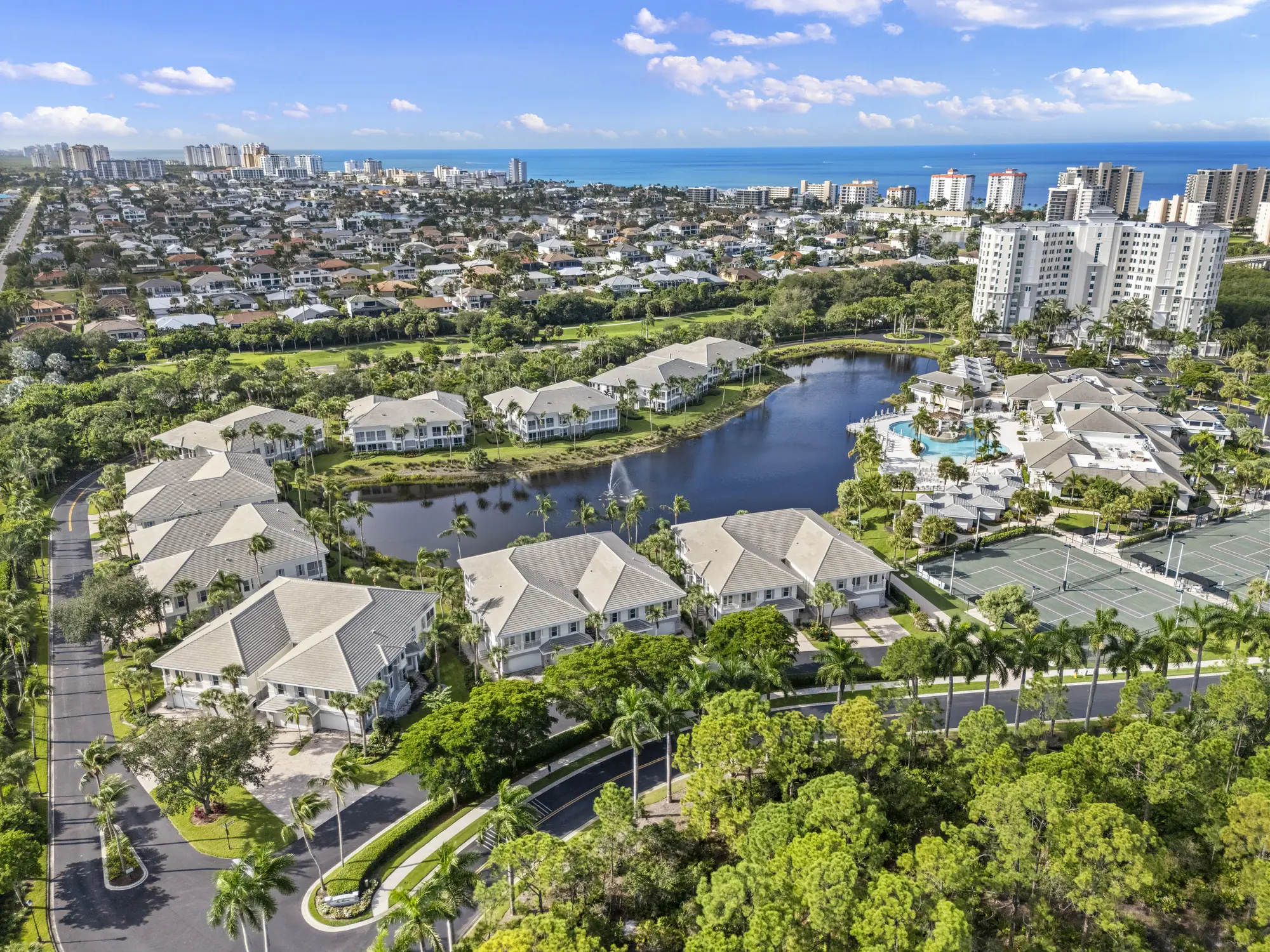 Aerial of the Sea Grove coach homes around the lake at The Dunes of Naples, with the Plantation Club, a Dunes tower and the Gulf beyond